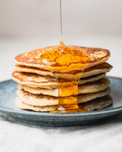 Load image into Gallery viewer, Stack of pancakes with hot honey being poured over them on a gray plate.
