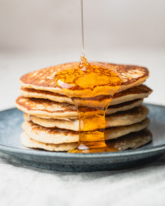 Stack of pancakes with hot honey being poured over them on a gray plate.